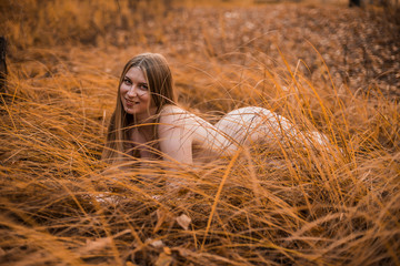 Young, sexy, plump naked girl with really big Breasts lying in the yellow grass in the forest. Autumn, overcast.