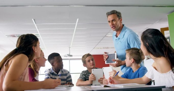 Teacher assisting schoolkids on digital tablet 