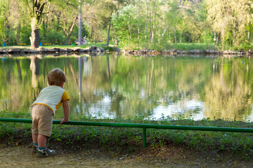 Fototapeta premium Small boy on the pond beach and looking around landscape