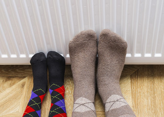 Feet in woolen winter socks warm their feet near heating radiator at home.