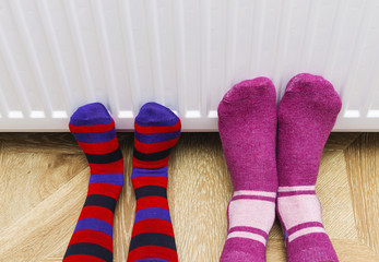 Woman and child wearing colorful pair of striped woolly socks warming cold feet in front of heating...