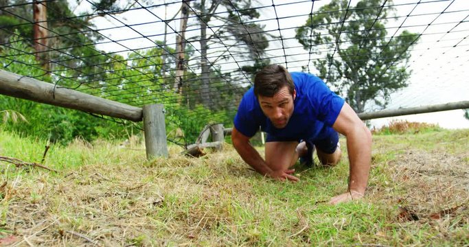 Fit man crawling under the net during obstacle course 