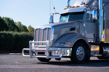 Hip powerful gray glossy big rig semi truck with grille guard and chrome accessories stand on truck...