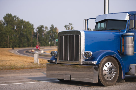 Classic blue big rig semi truck with chrome accessories running on the road