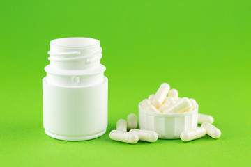 Close up white pill bottle with spilled out pills and capsules in cap on green background with copy space. Focus on foreground, soft bokeh. Pharmacy drugstore concept
