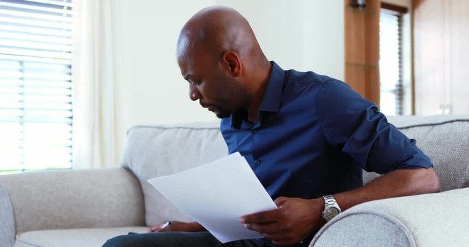 Man calculating invoices on mobile phone in living room 