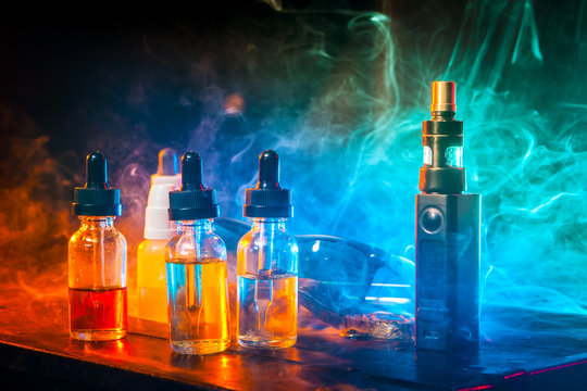 Liquids for paper. Liquid for electronic cigarettes. Vape the Concept. Smoke clouds and vape liquid bottles on dark background