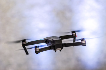 The flight of a black unmanned quadrocopter on a light blurred background.