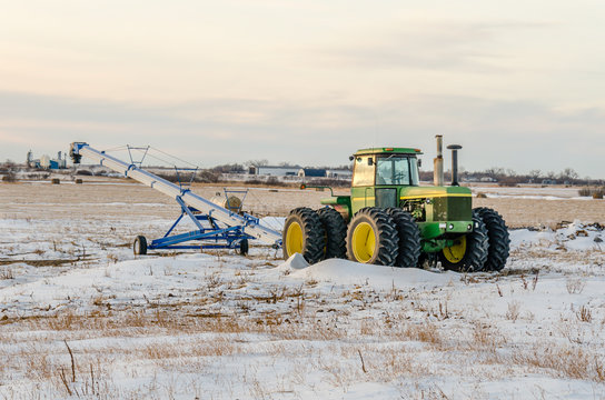 Green tractor and grain loader on the snow field