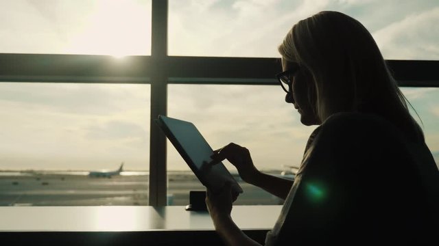 Silhouette of a woman using a tablet by the airport terminal window. Always online, travel apps
