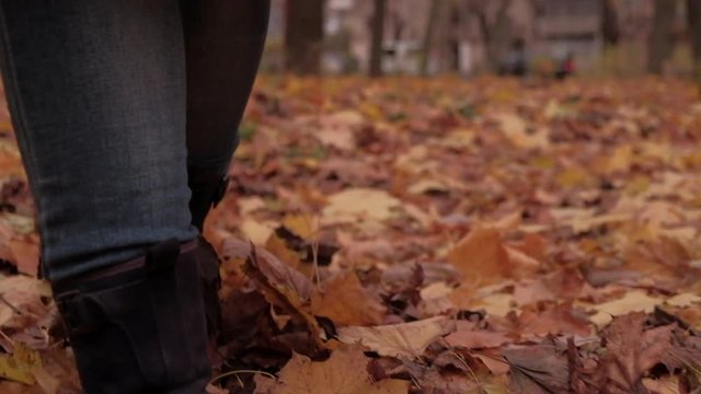 Camera follows behind boots of woman walking through autumn leaves. Shot in slow motion