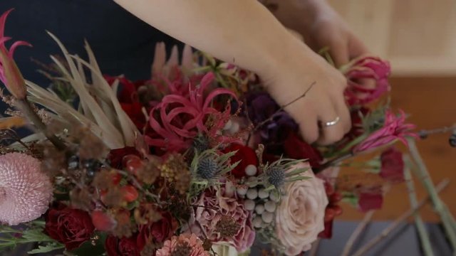 Young woman creates beautiful bouquet in store workshop. Female fills neatly flower composition, inserting fresh blossoms inside. Talented specialist knows all about varieties of flowers