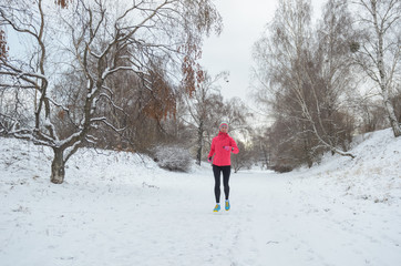 Winter running in park: happy active woman runner jogging in snow, outdoor sport and fitness concept
