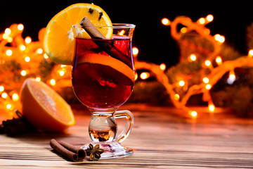 Christmas hot mulled wine in a glass with spices, anise, slice of orange and cinnamon sticks on Christmas lights background