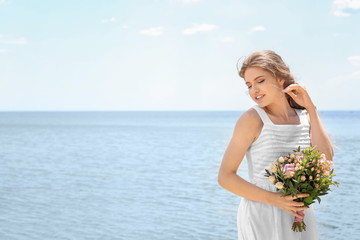 Fototapeta na wymiar Young bride in white gown holding bouquet on seashore