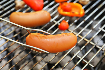 Tongs holding sausage near barbecue grill