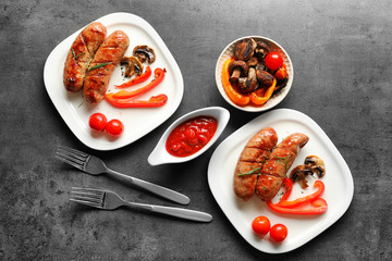 Composition with grilled sausages, vegetables and sauce on grey background