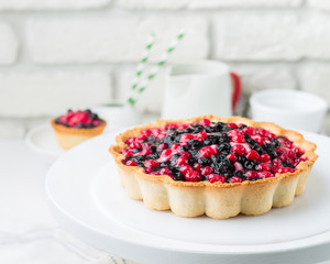 Tart  with cream and berries in a cafe. A modern cake with a cut piece. Light background, white brick wall, light dishes and cake stand. The atmosphere of the coffee house. 