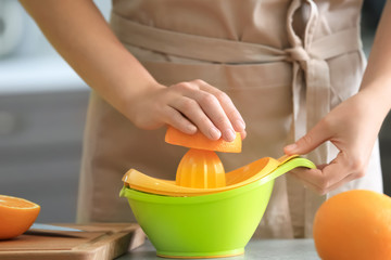 Woman squeezing juice from ripe orange in kitchen