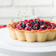 Tart  with cream and berries in a cafe. A modern cake with a cut piece. Light background, white brick wall, light dishes and cake stand. The atmosphere of the coffee house. 