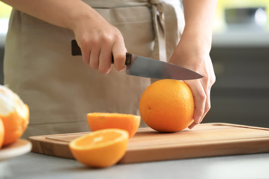 Woman cutting ripe orange in kitchen