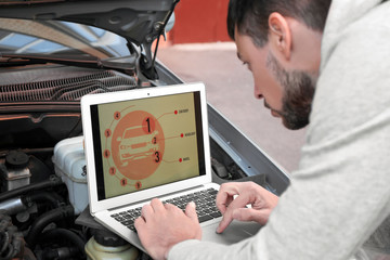 Young male mechanic using computer diagnostic while repairing car