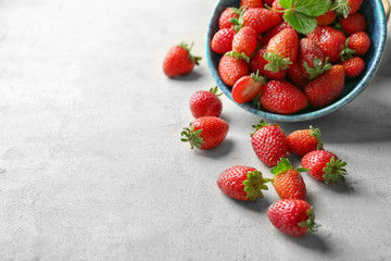 Fresh ripe strawberries scattered from bowl on table