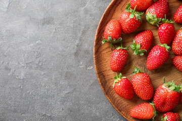 Wooden plate with fresh strawberries on grey background