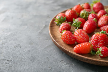 Wooden plate with fresh strawberries on grey background