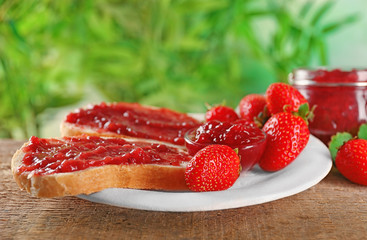 Plate with pieces of bread and strawberry jam on wooden table