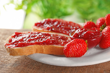 Plate with pieces of bread and strawberry jam on wooden table