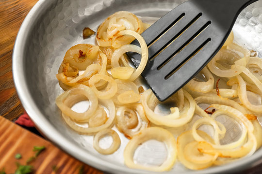 Pan with spatula and fried onion on table