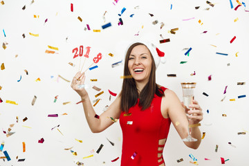 Beautiful smiling caucasian young happy woman in red dress and Christmas hat standing with card number 2018 and glass of champagne on white background confetti. Santa girl isolated. New Year holiday