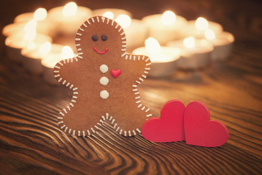 Gingerbread man with hearts and candles on wooden background