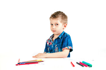 Young cute boy wearing a blue shirt with colored pencils on a white background. The concept of...