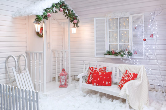 Winter Exterior Of A Country House With Christmas Decorations In The American Style. Snow-covered Courtyard With A Porch, Tree And Wooden Vintage Sleds.