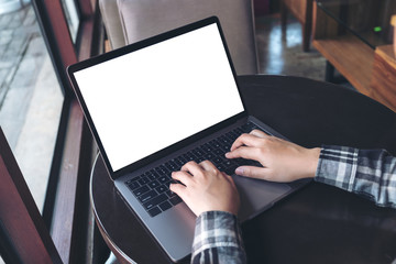 Mockup image of business woman using and typing on laptop with blank white screen on wooden table in cafe