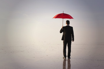 Businessman in black suit with a red umbrella on salt lake