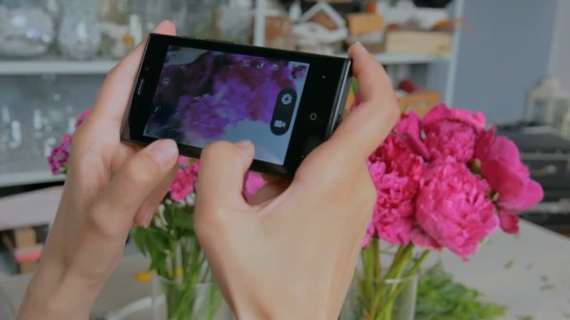 Professional floral artist, florist taking photo of her beautiful bouquet of pink peonies with smartphone. Close up shot of woman's hands with mobile. Photography, technology and social media concept