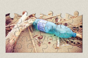Empty green plastic bottle abandoned on the beach - concept image in jigsaw puzzle shape
