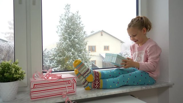 Video. Portrait of happy girl surprising her gifts at the window. It is snowing