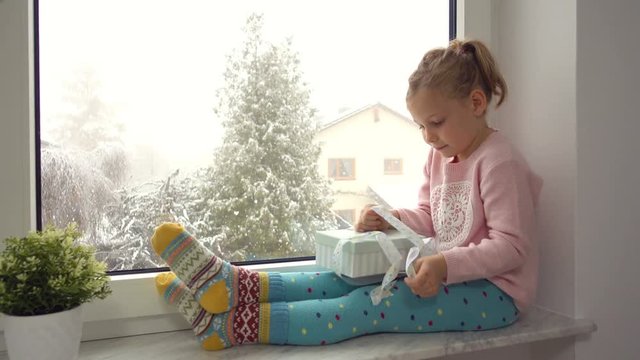 Video. Portrait of happy girl surprising her gifts at the window. It is snowing