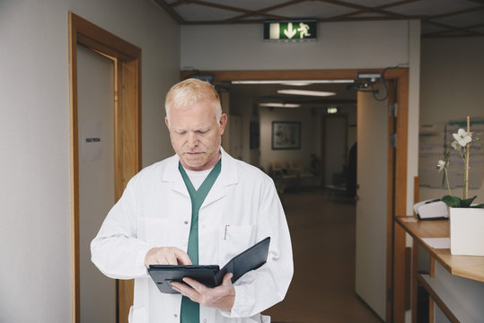 Mature doctor using digital tablet while standing in hospital corridor