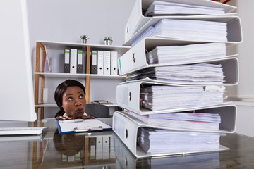 Woman Looking At Stack Of Folders On Desk