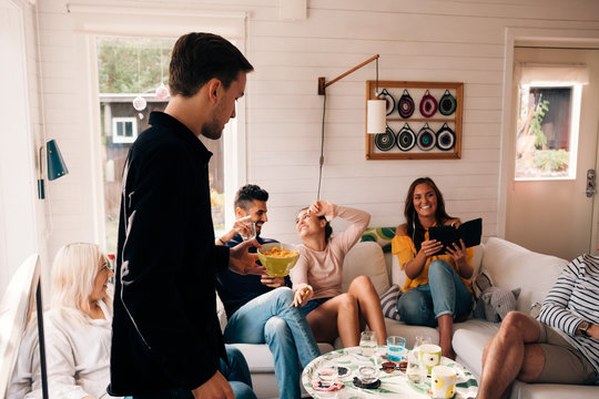 Young man holding bowl of snack while friends enjoying in cottage