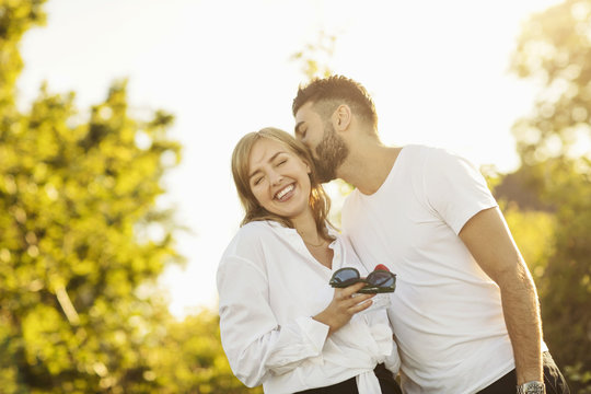 Loving man kissing girlfriend while standing against clear sky