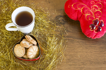 Valentines decoration on wooden background. Mug of red tea, cookies and red valentines heart on wooden background.