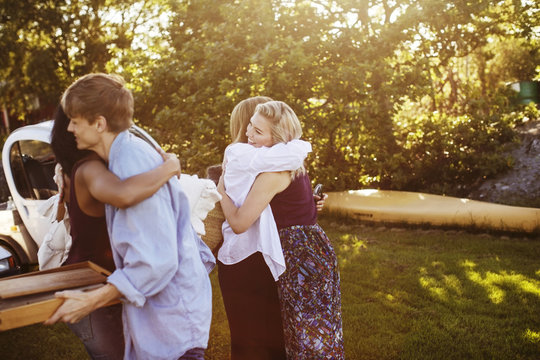 Happy male and female friends embracing while standing against trees at garden