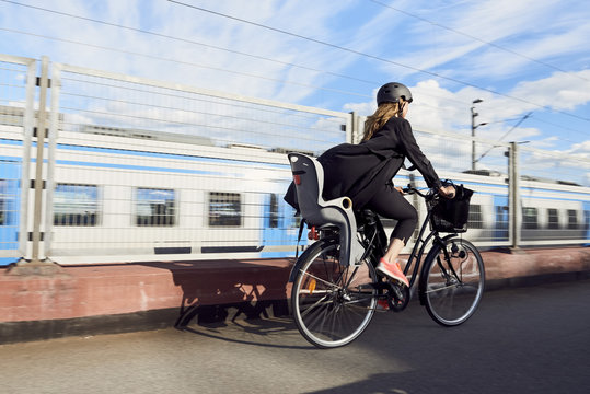 Rear view of mature woman cycling on road by fence against sky