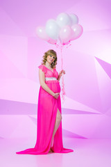 Beautiful and happy pregnant woman standing in studio with balloons on pink background.